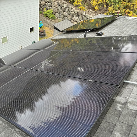 Technician rinsing rooftop solar panels on a port orchard home under cloudy skies